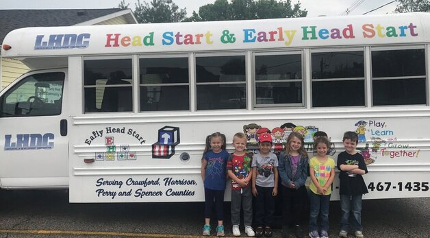 Head start students smiling by a bus